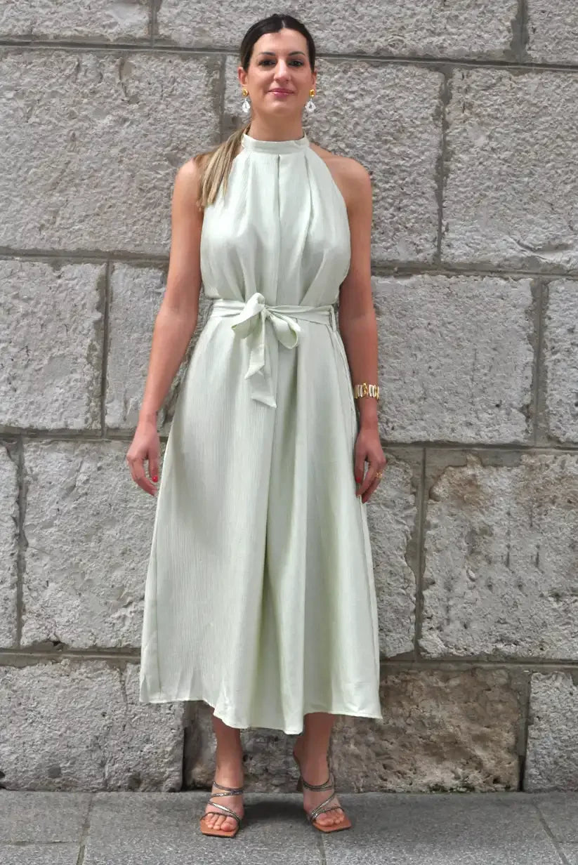 Mujer con vestido fluido verde agua cuello halter primavera verano, fondo de pared de piedra