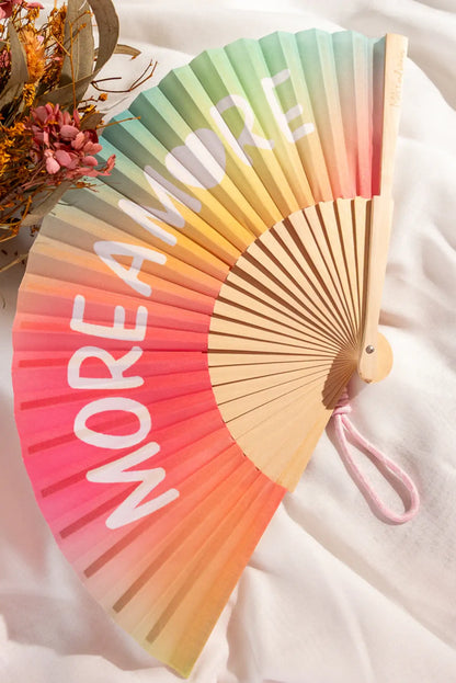 Abanico de madera con gradiente de colores y texto 'MORE AMORE', ideal como complemento de moda femenina casual.