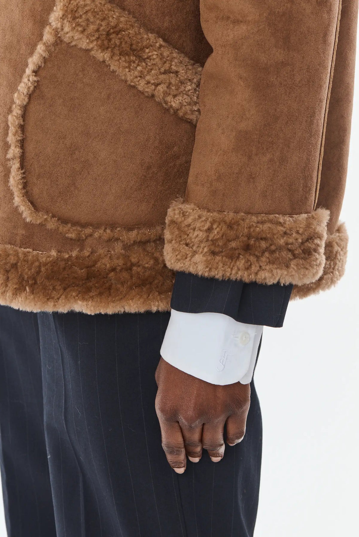 Detalle de chaqueta de piel marrón con forro de borreguito y pantalón de vestir azul marino.