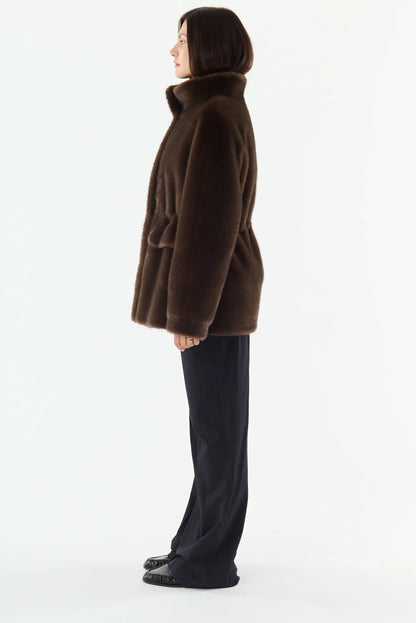 Mujer de perfil vistiendo un abrigo de piel sintética marrón y pantalones anchos negros