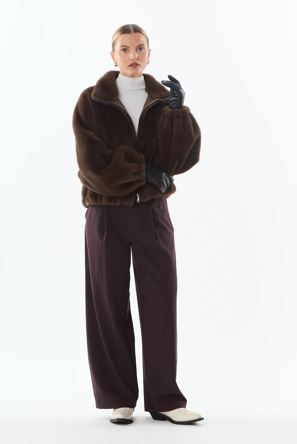 Mujer con chaqueta de piel sintética marrón, pantalones anchos burdeos y guantes negros.