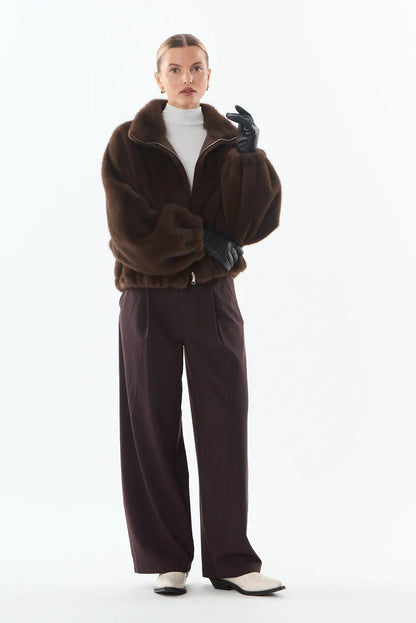 Mujer con chaqueta de piel sintética marrón, pantalones anchos burdeos y guantes negros.