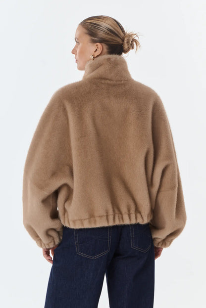 Mujer de espaldas luciendo chaqueta de pelo sintético color camel y vaqueros oscuros.