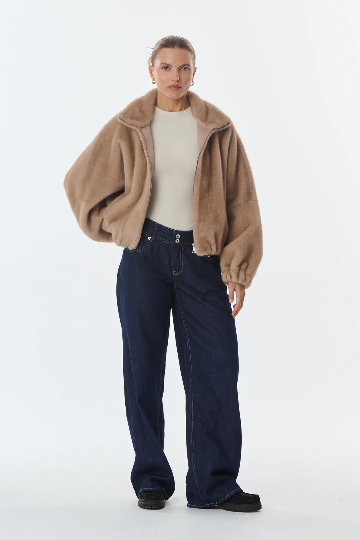Mujer con chaqueta de pelo sintético beige, camiseta blanca y vaqueros anchos azul oscuro.