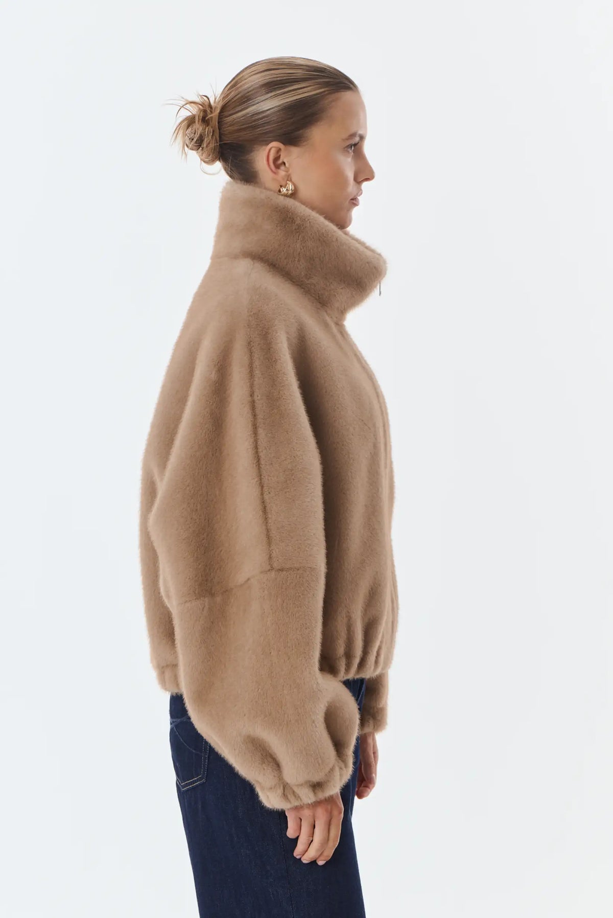 Mujer de perfil vistiendo chaqueta de pelo sintético color beige y pantalones vaqueros oscuros