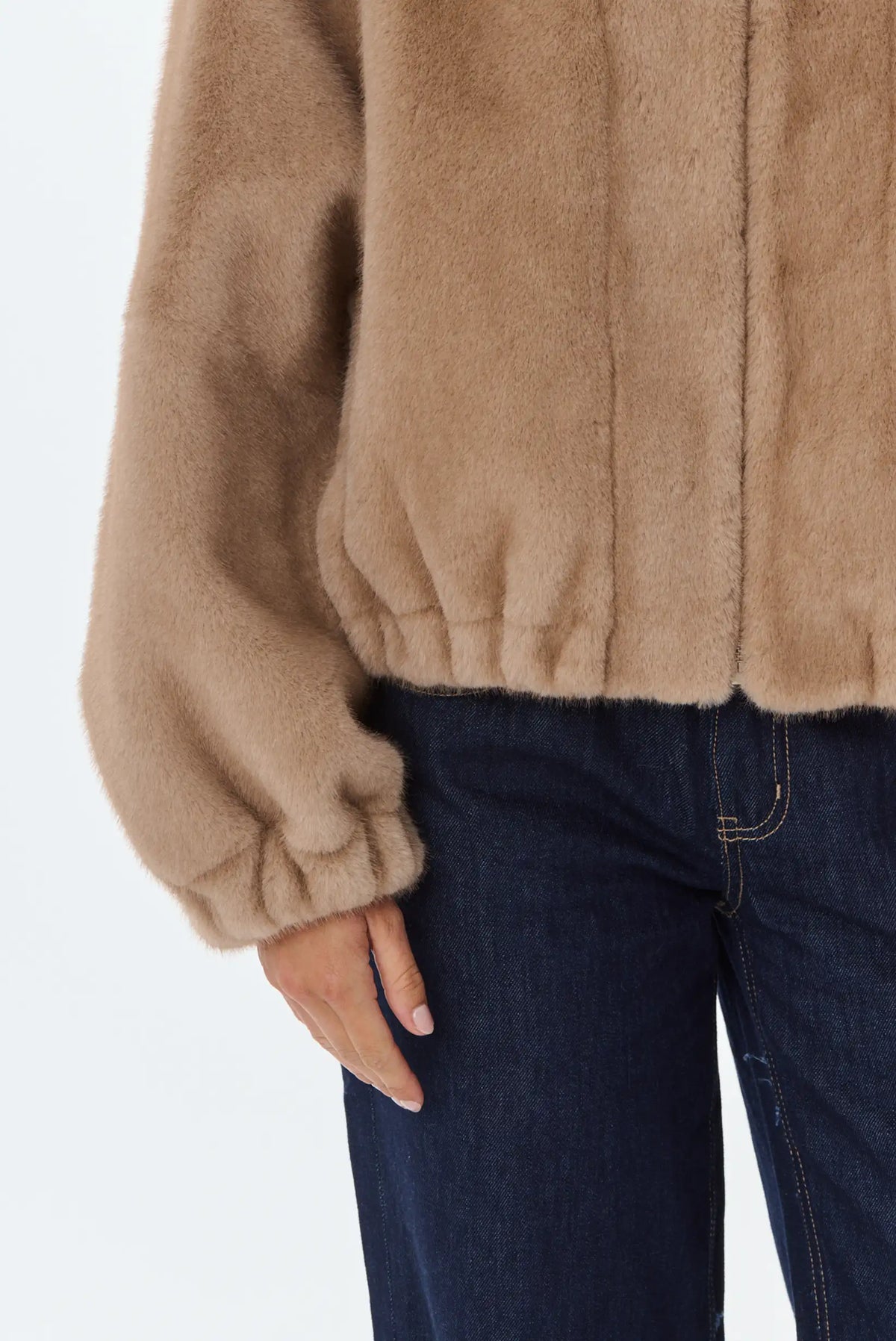 Primer plano de chaqueta de pelo sintético color camel y vaqueros oscuros.