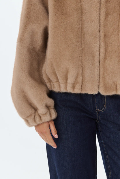 Primer plano de chaqueta de pelo sintético color camel y vaqueros oscuros.
