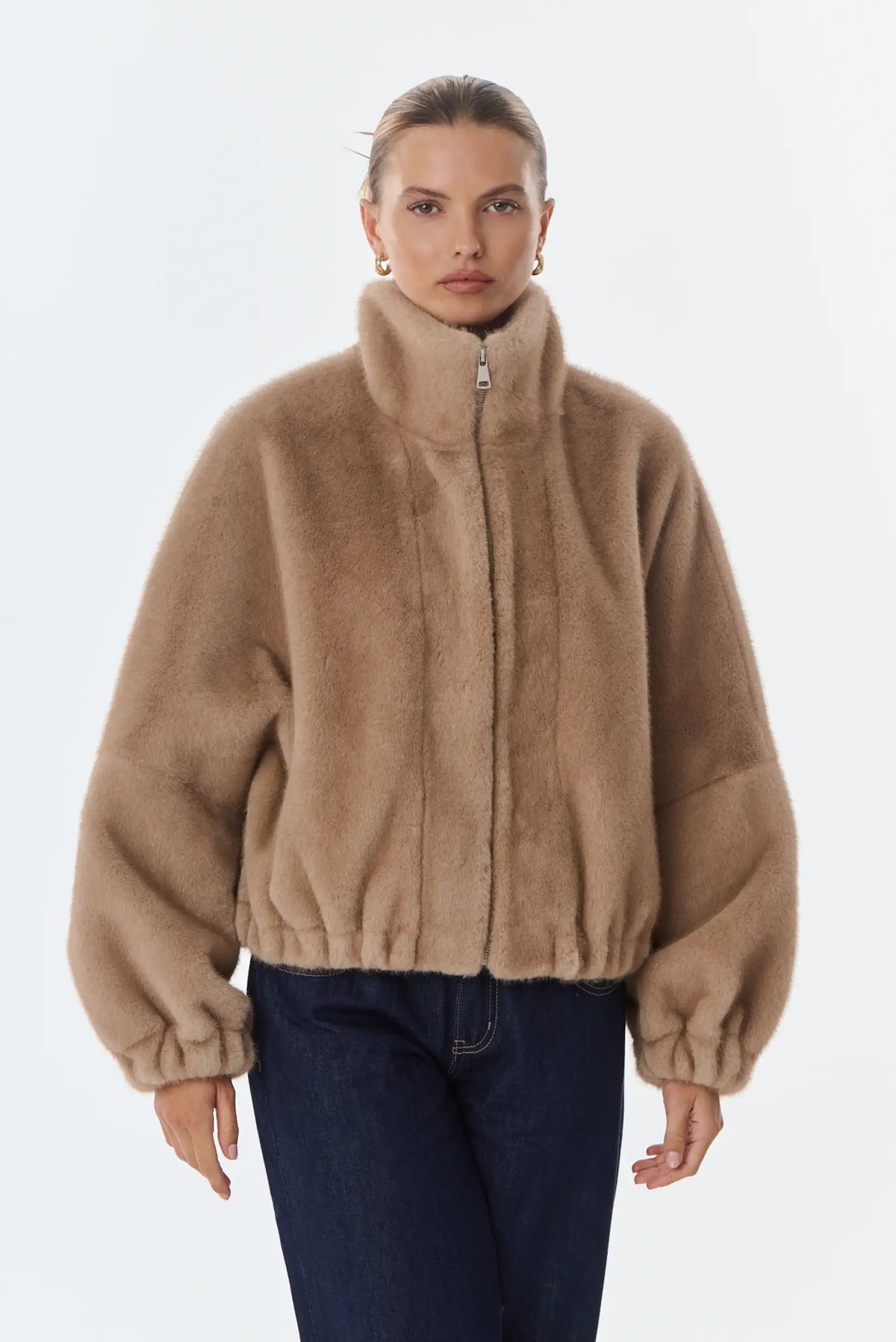 Mujer vistiendo chaqueta corta de pelo sintético color beige con cuello alto y vaqueros oscuros.