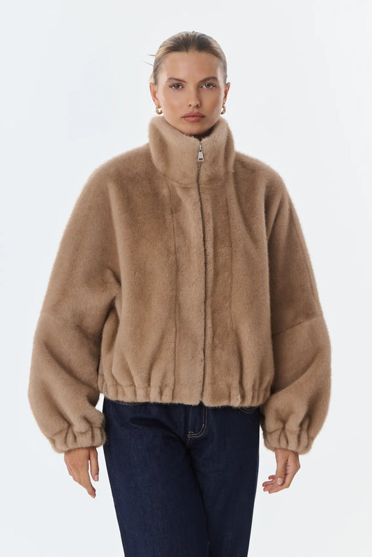 Mujer vistiendo chaqueta corta de pelo sintético color beige con cuello alto y vaqueros oscuros.
