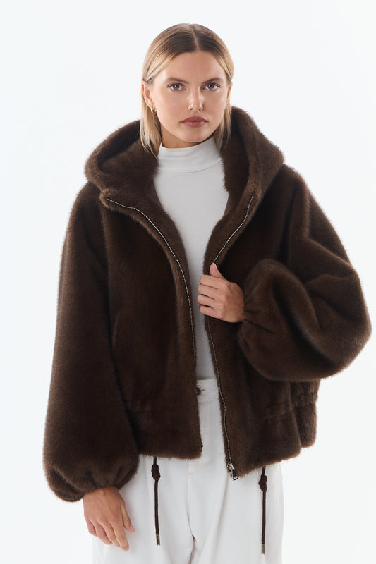 Mujer joven con chaqueta de pelo sintético marrón, capucha y cuello alto blanco