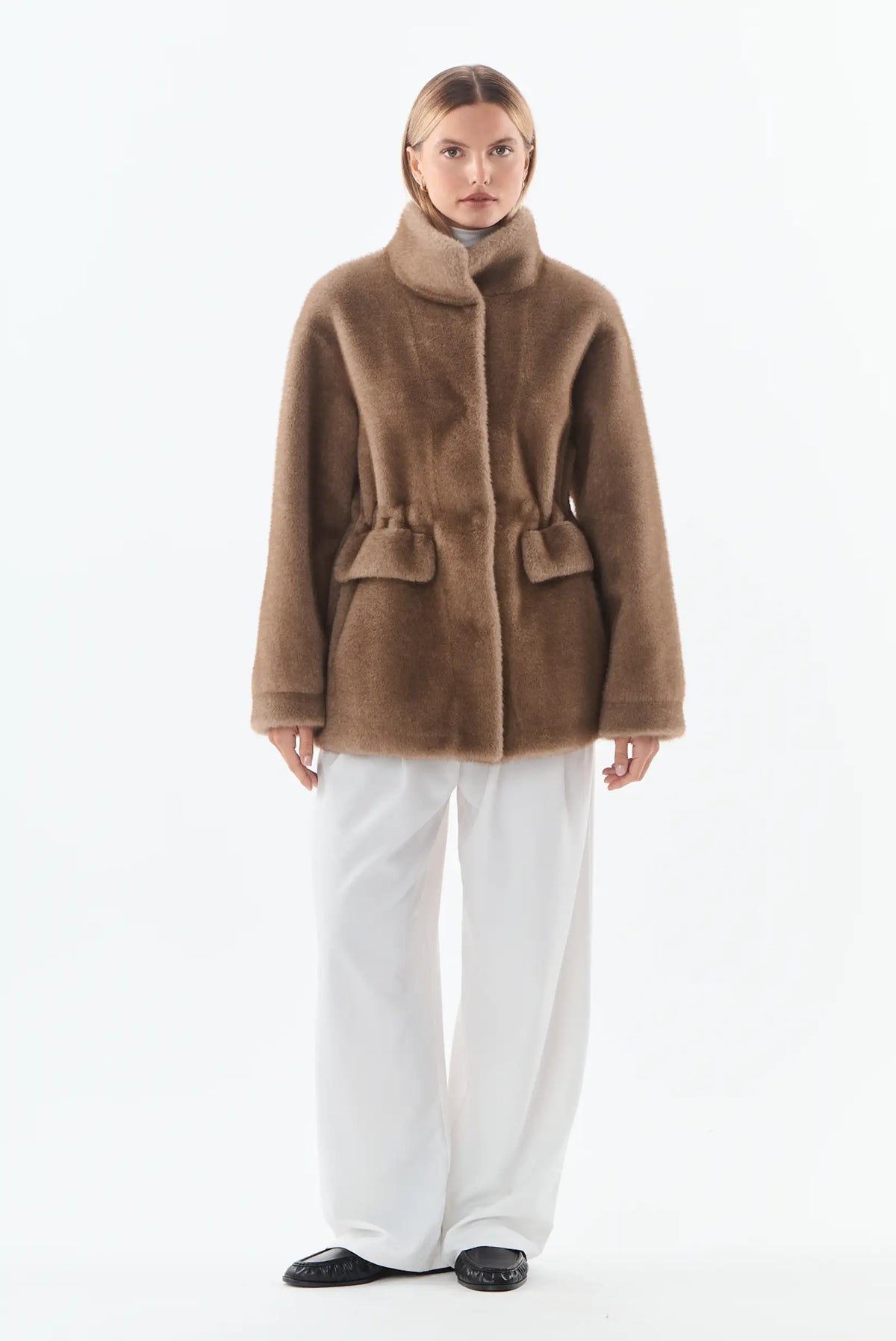 Mujer vistiendo abrigo de pelo marrón con pantalones anchos blancos y zapatos negros.