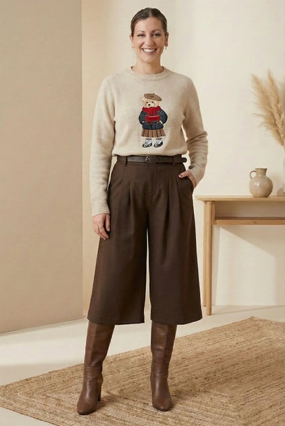 Mujer sonriente con suéter beige estampado oso y bermuda marrón chocolate acompañada de botas altas marrones