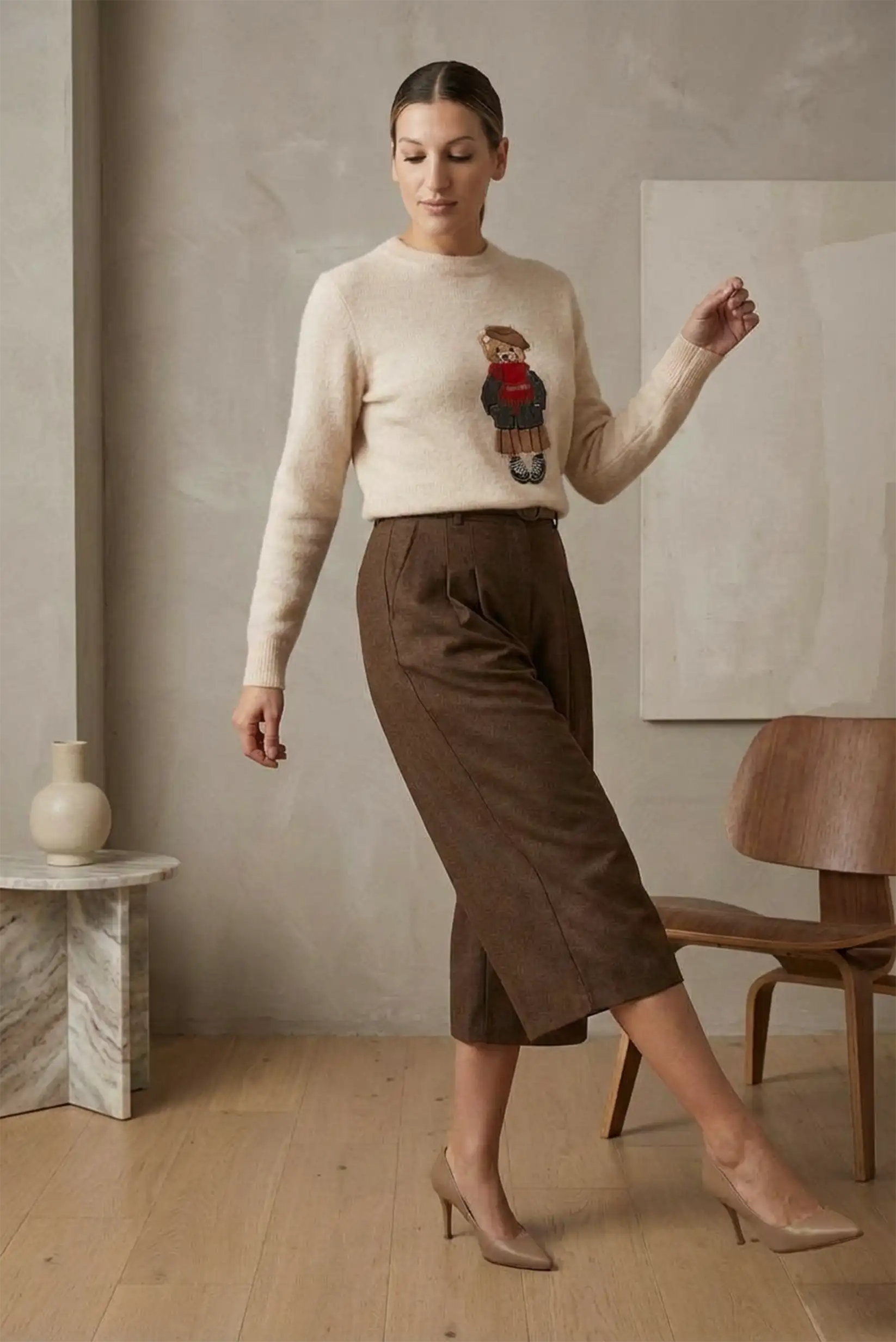 Mujer con jersey beige y bermuda marrón larga de invierno, tacones nude, interior minimalista