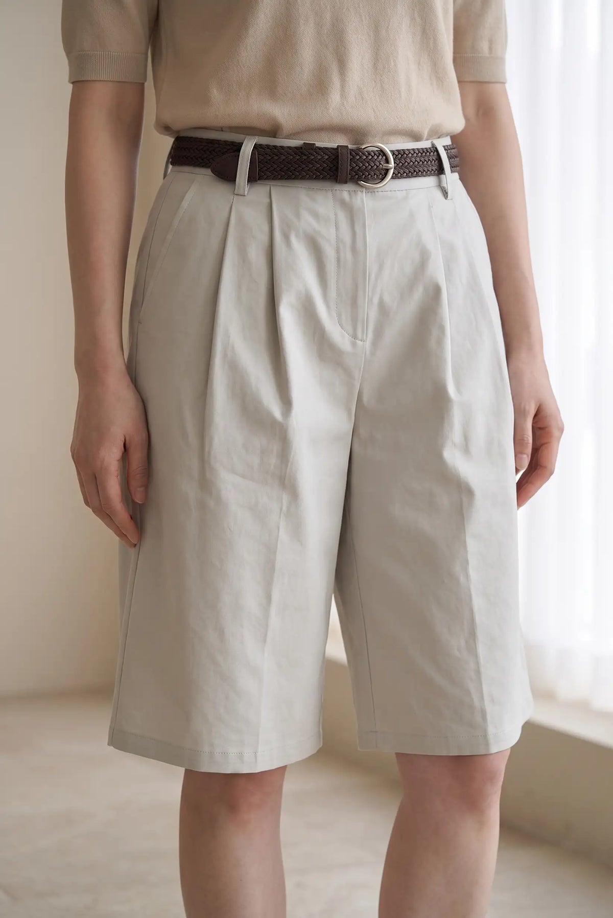 Mujer vistiendo bermudas beige de pinzas con cinturón marrón trenzado