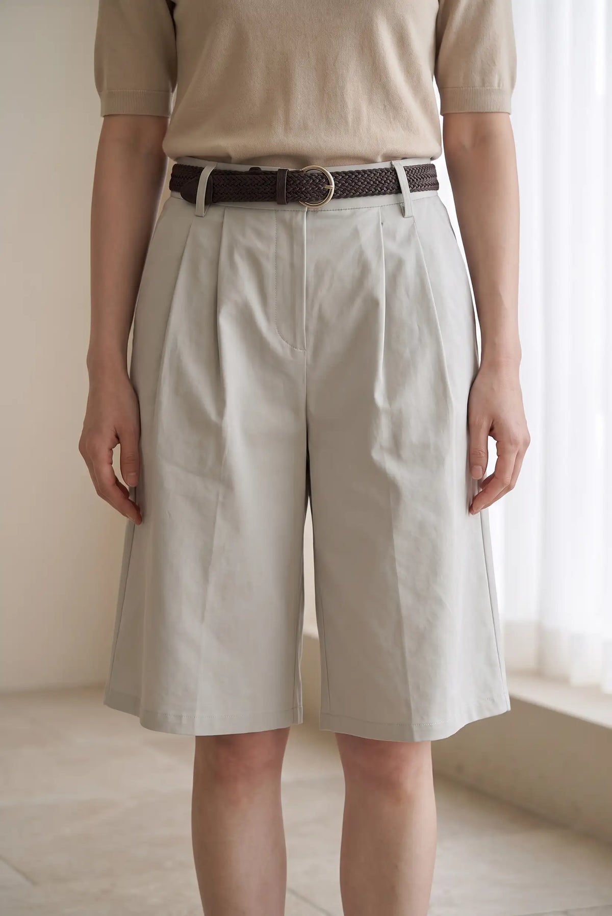 Mujer vistiendo pantalones cortos beige de pinzas con cinturón marrón trenzado