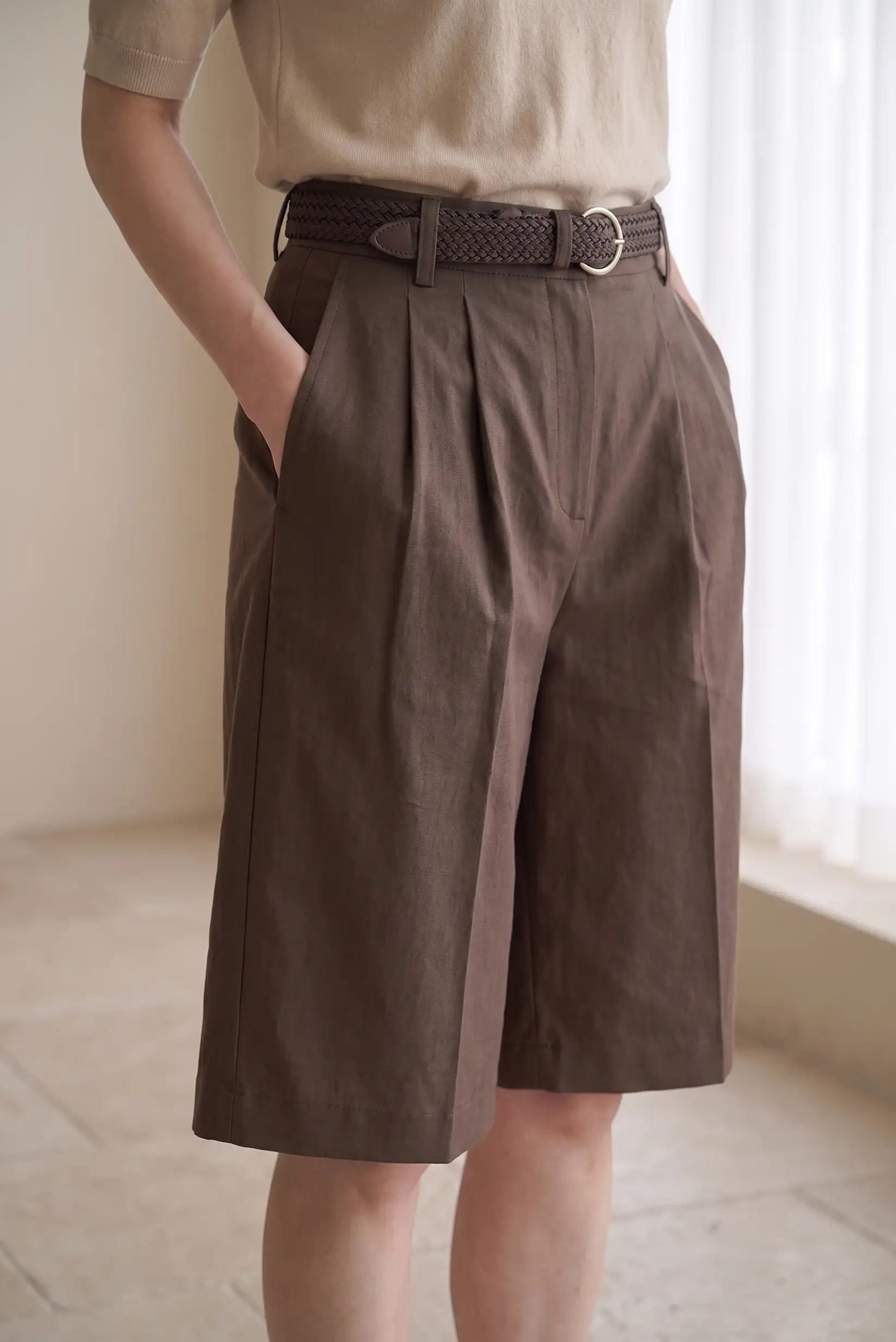 Mujer vistiendo bermudas marrones de talle alto con pinzas y cinturón trenzado