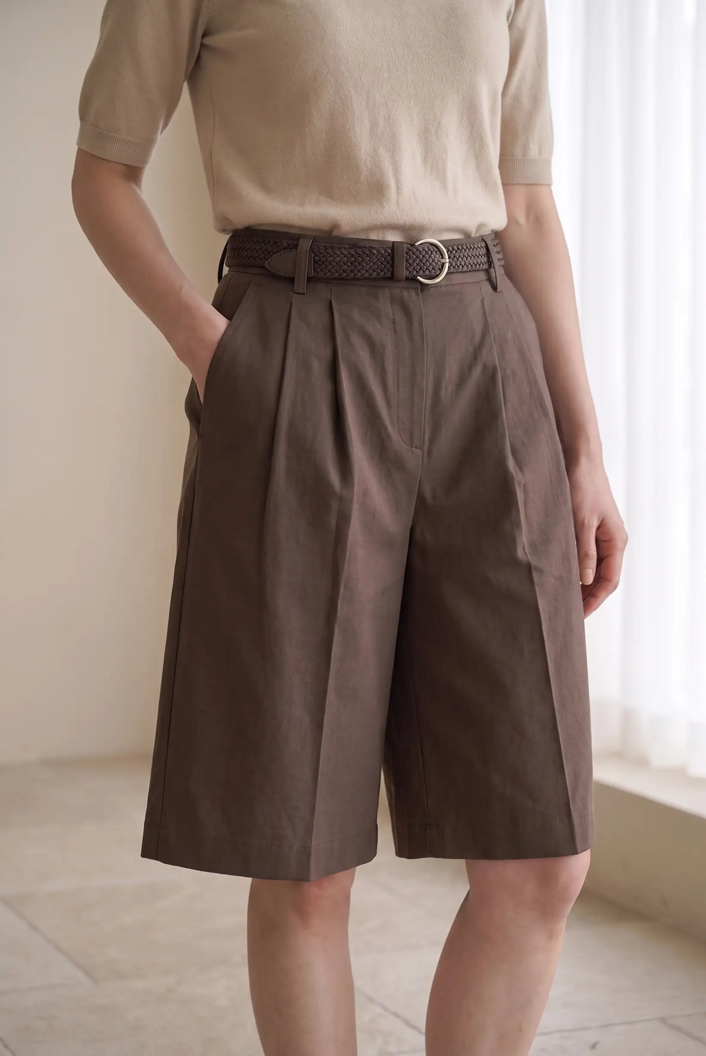 Mujer vistiendo pantalones cortos marrones con pinzas y cinturón trenzado