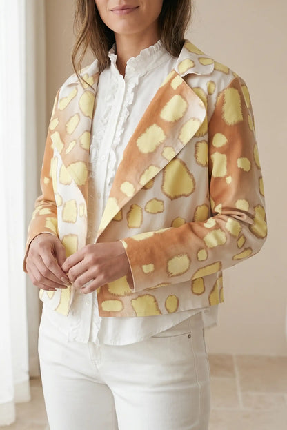 Mujer con blazer estampado de manchas amarillas y marrones, blusa y pantalón blanco.
