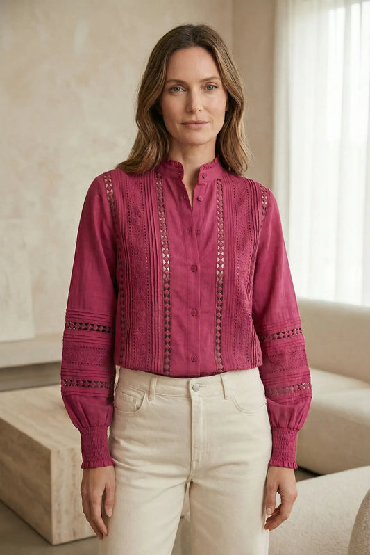 Mujer con blusa rosa de manga larga y detalles calados, estilo primavera, en sala moderna.