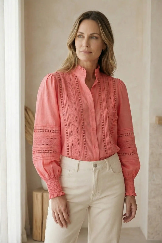 Mujer con blusa coral de manga larga, bordados primaverales y pantalón claro, moda casual femenina.