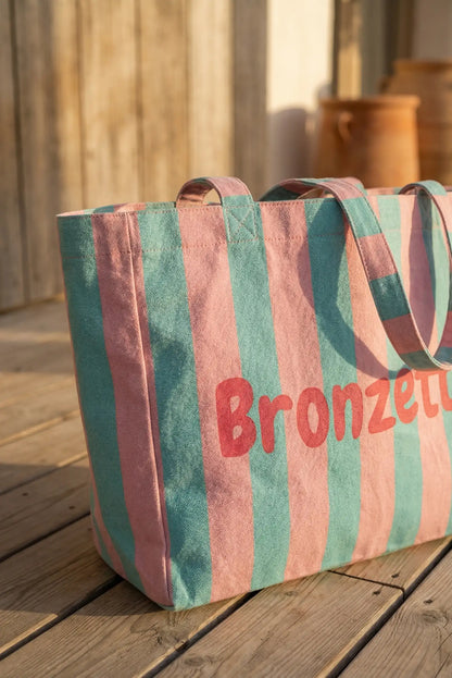 Bolsa de tela con rayas verdes y rosas, ideal para playa o piscina, sobre madera.
