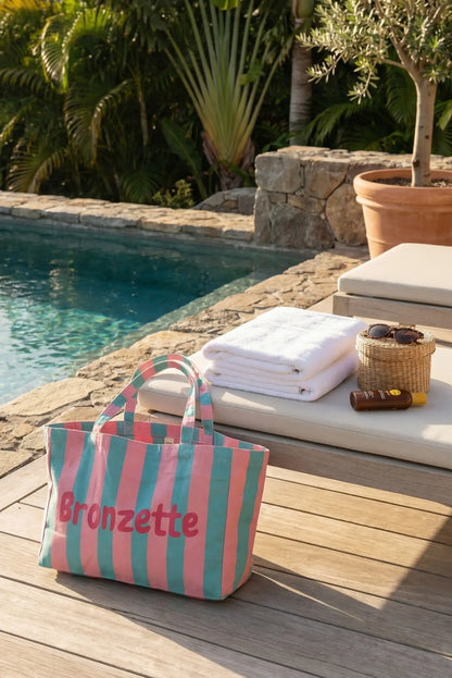 Bolsa de tela rayas rosa y verde junto a piscina, ideal para playa o verano.