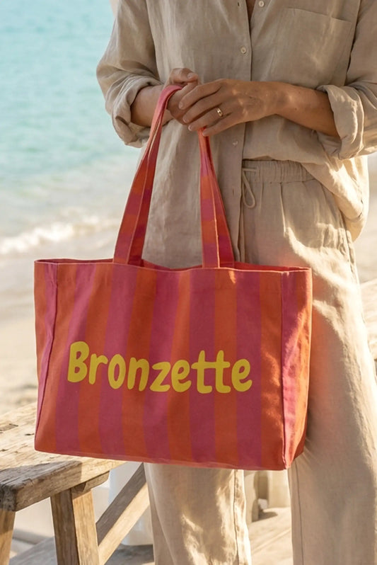 Bolsa de tela rayas rojas y rosas con texto Bronzette, ideal para playa o piscina, junto al mar.