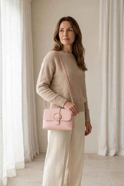 Mujer con bolso bandolera pequeño rosa, cierre dorado, outfit casual y elegante.