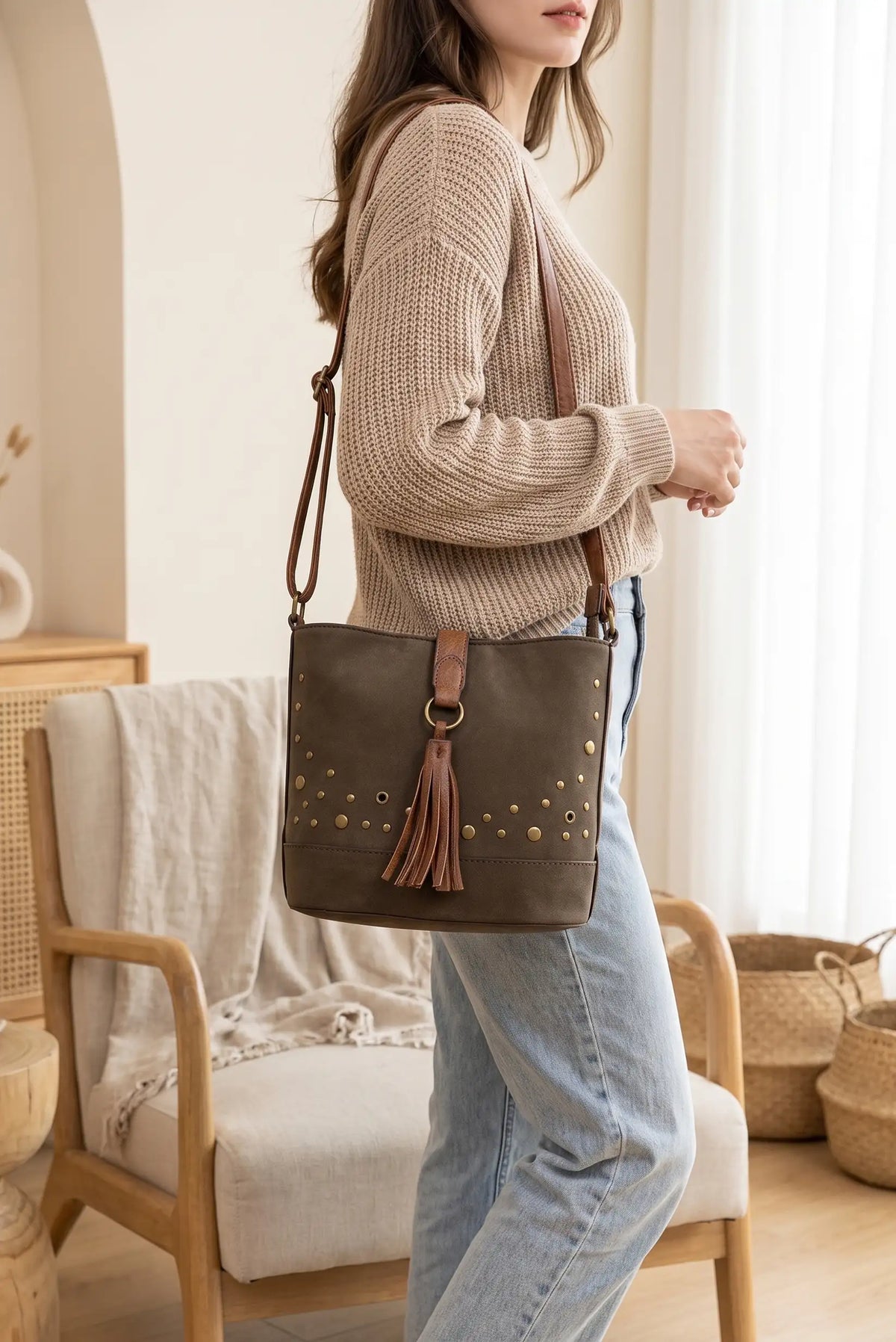 Mujer con bolso bandolera de cuero marrón con borla y tachuelas sobre jersey beige y vaqueros