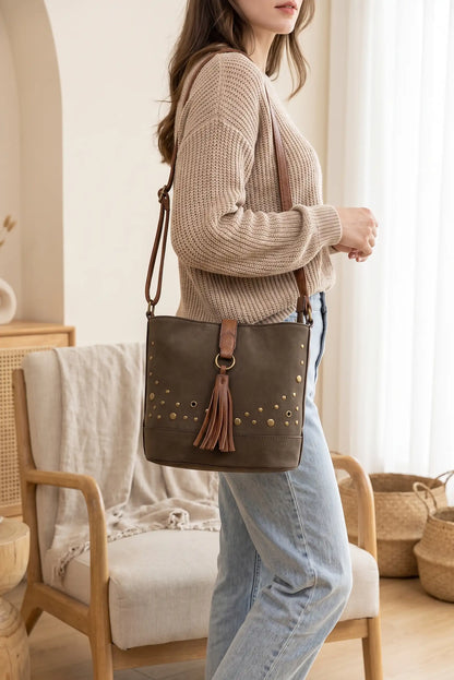 Mujer con bolso bandolera de cuero marrón con borla y tachuelas sobre jersey beige y vaqueros