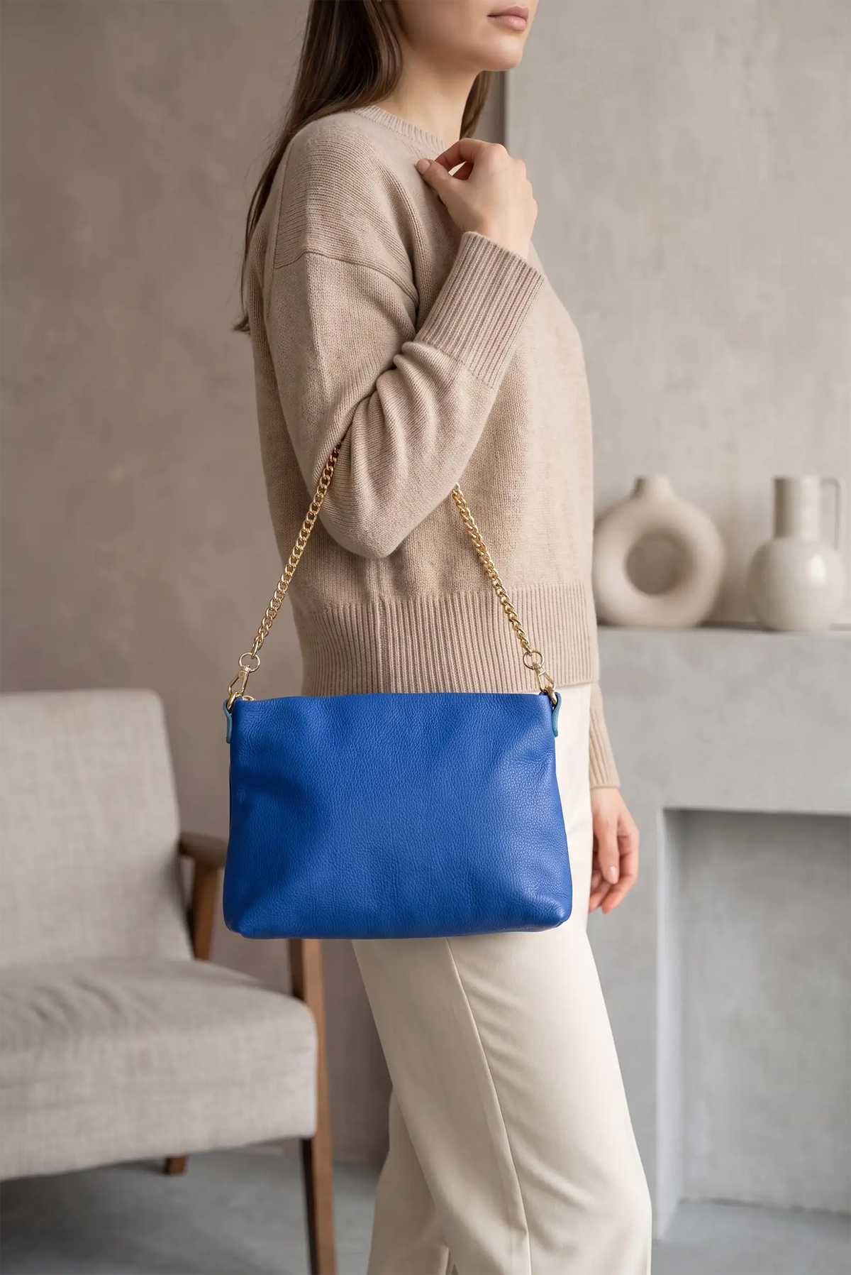 Mujer con jersey beige y pantalón blanco llevando un bolso azul eléctrico con cadena dorada