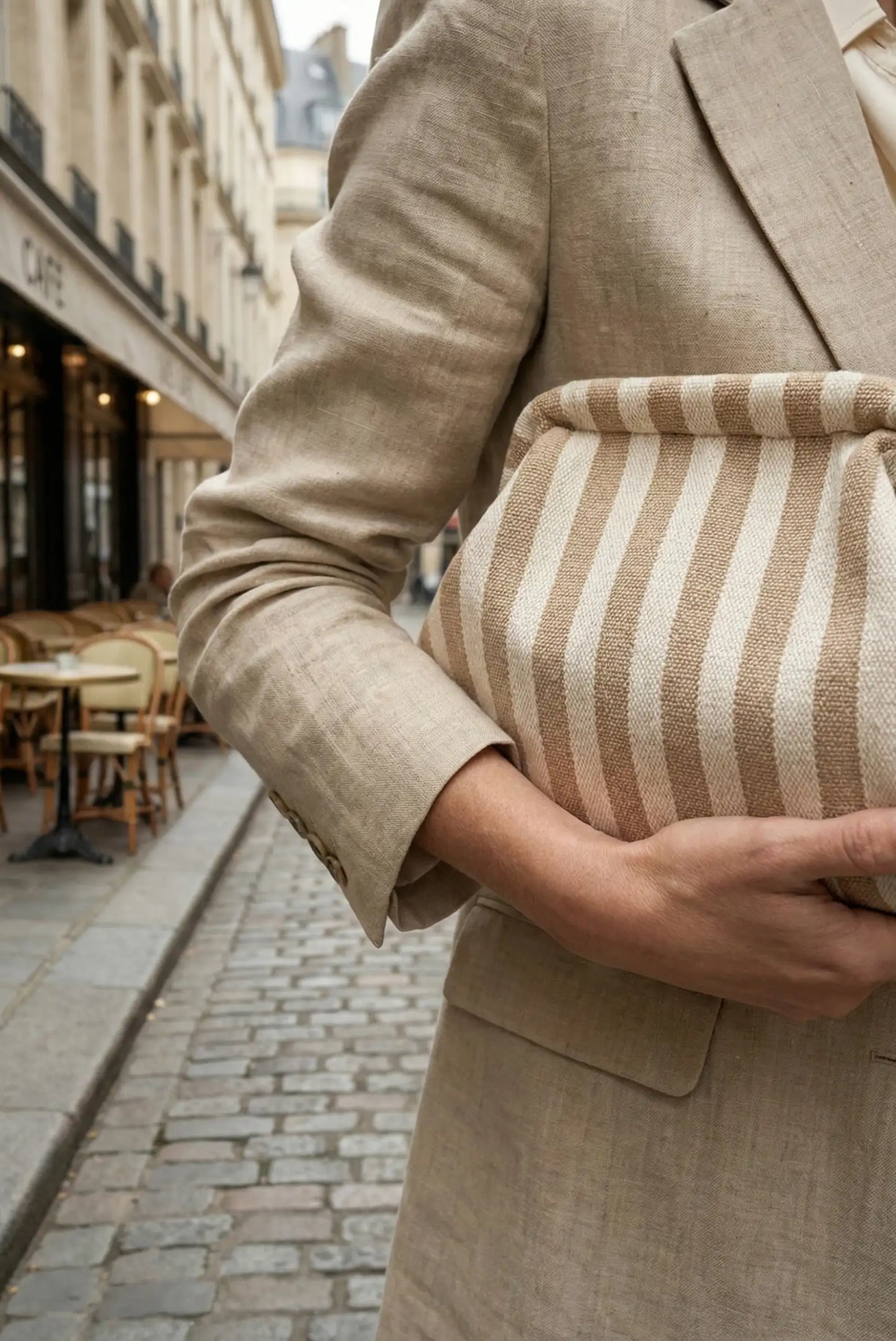 Bolso clutch de rayas beige y blanco, estilo parisino, sostenido por mujer con blazer beige