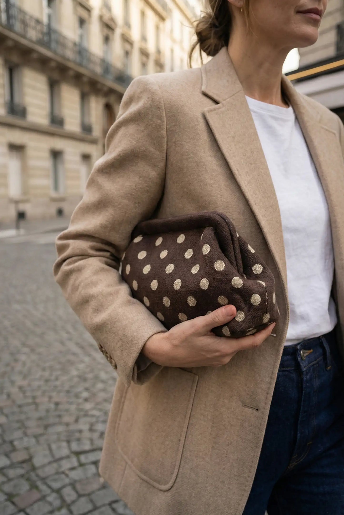 Clutch marrón chocolate con topos beige, estilo parisino, llevado por mujer con blazer beige