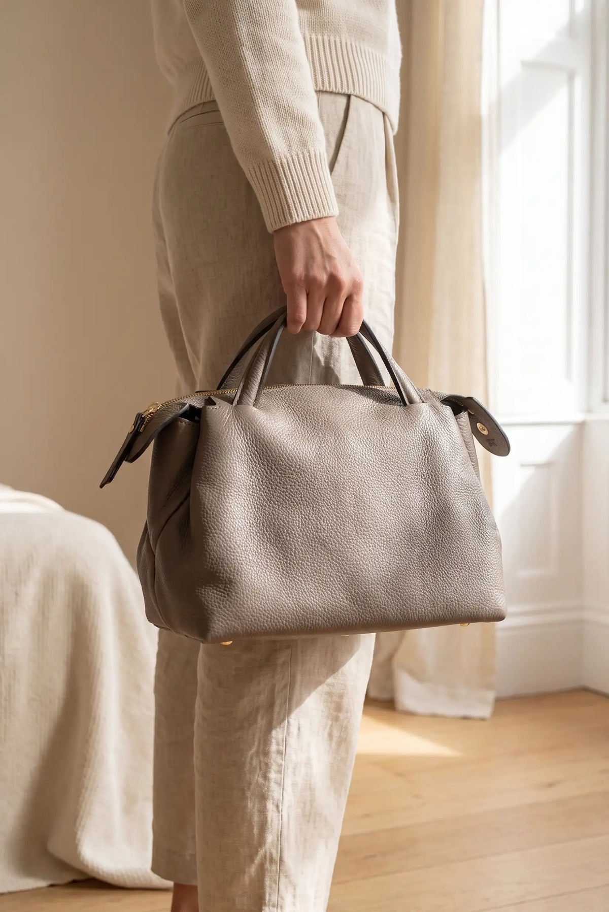 Mujer sosteniendo un bolso de mano de cuero granulado en color topo.