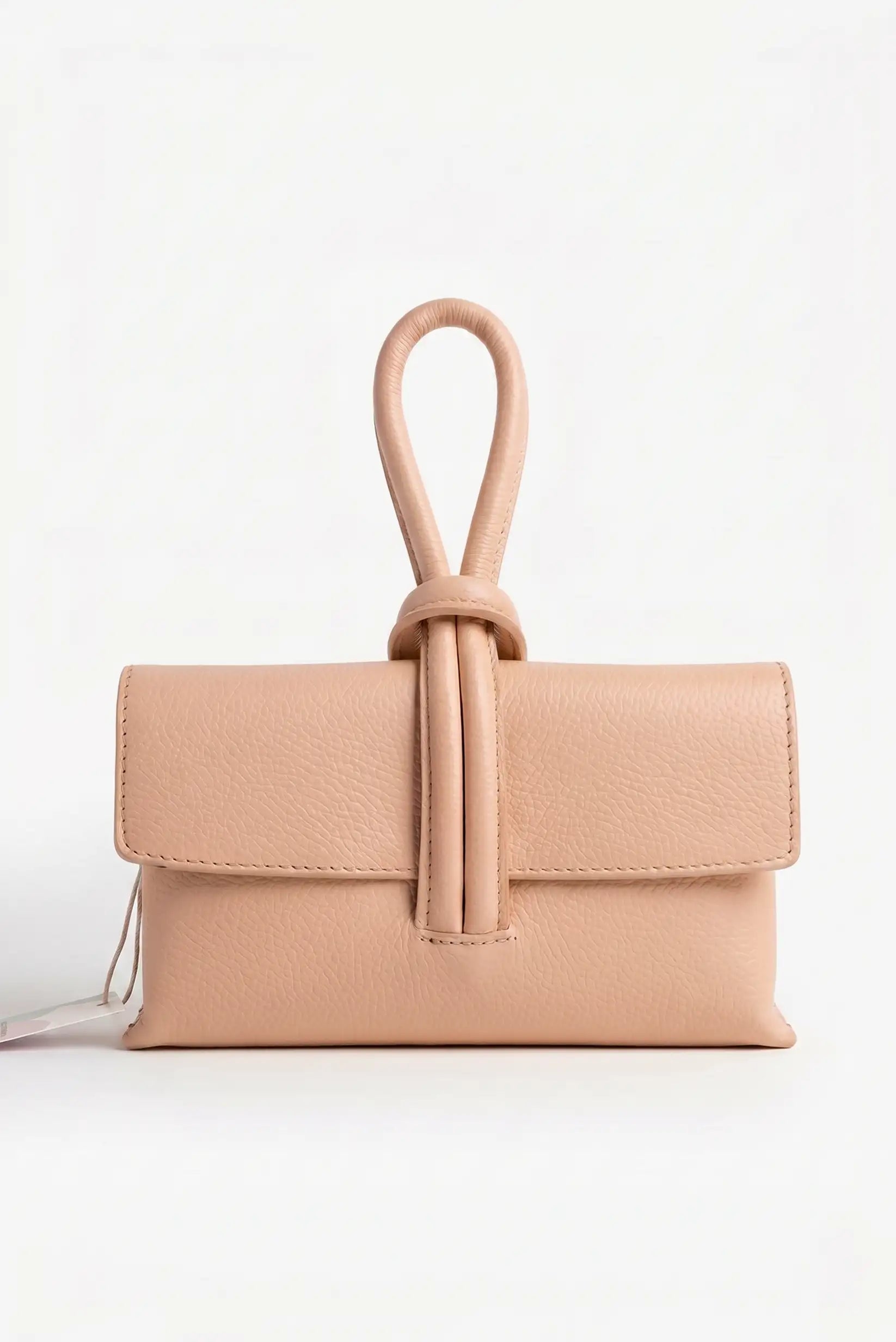 Bolso de mano pequeño nude de piel con asa tipo nudo, fondo blanco, estilo casual elegante