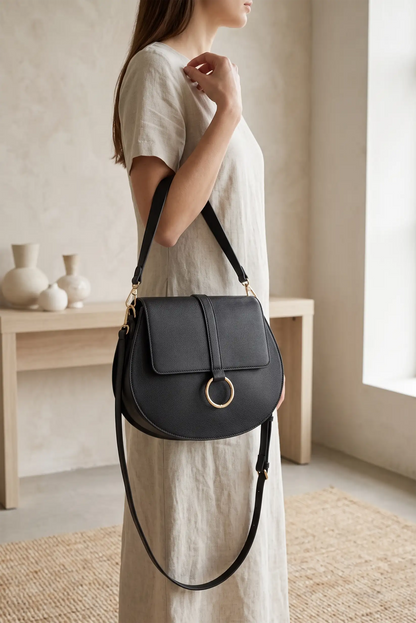Mujer con vestido beige llevando un bolso bandolera negro de cuero con detalle de anillo dorado