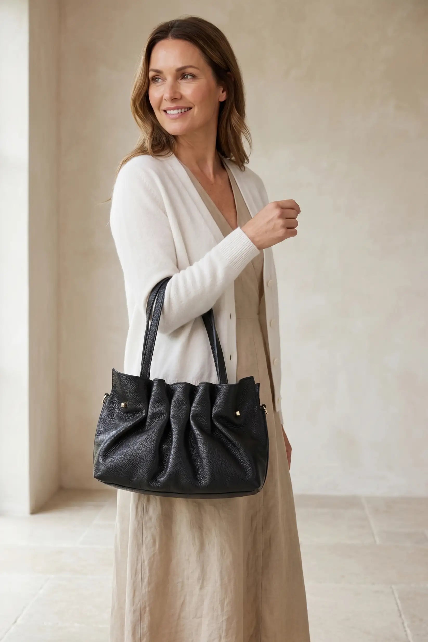 Bolso de mano de piel negra estilo acordeón, elegante y casual, llevado por mujer.