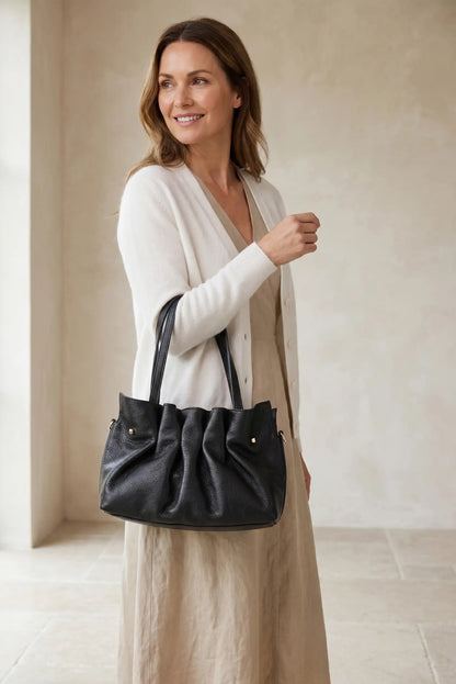 Bolso de mano de piel negra estilo acordeón, elegante y casual, llevado por mujer.