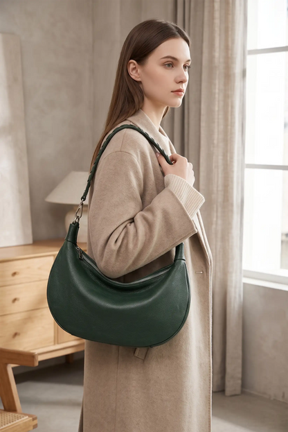 Mujer con abrigo beige llevando un bolso hobo de piel en color verde oscuro.