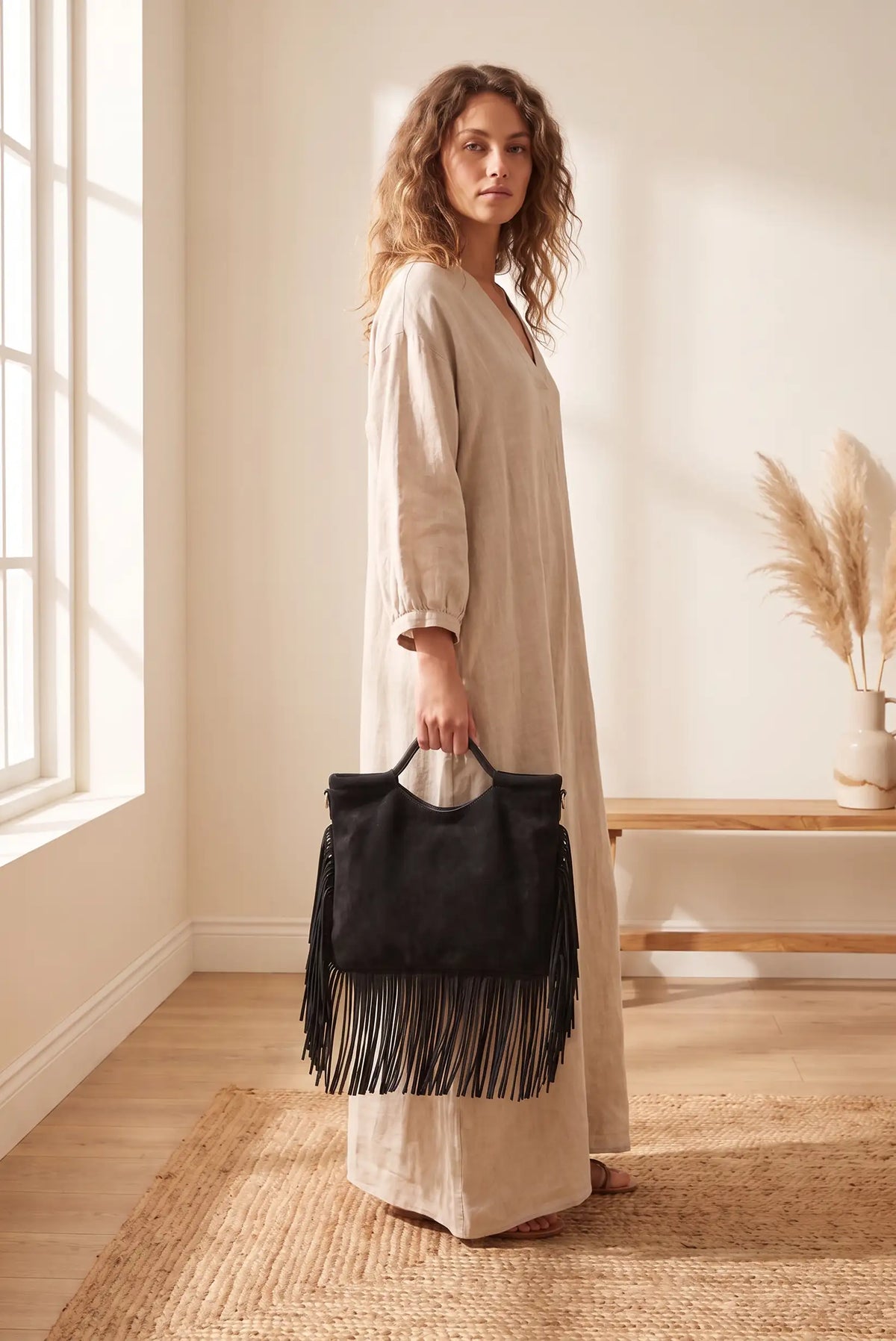 Mujer con vestido beige sosteniendo un bolso negro tipo ante con flecos de CHICA del Sur.