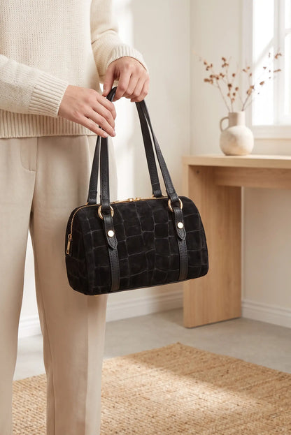 Mujer sosteniendo un bolso negro de CHICA del Sur con efecto cocodrilo y acabado tipo ante.