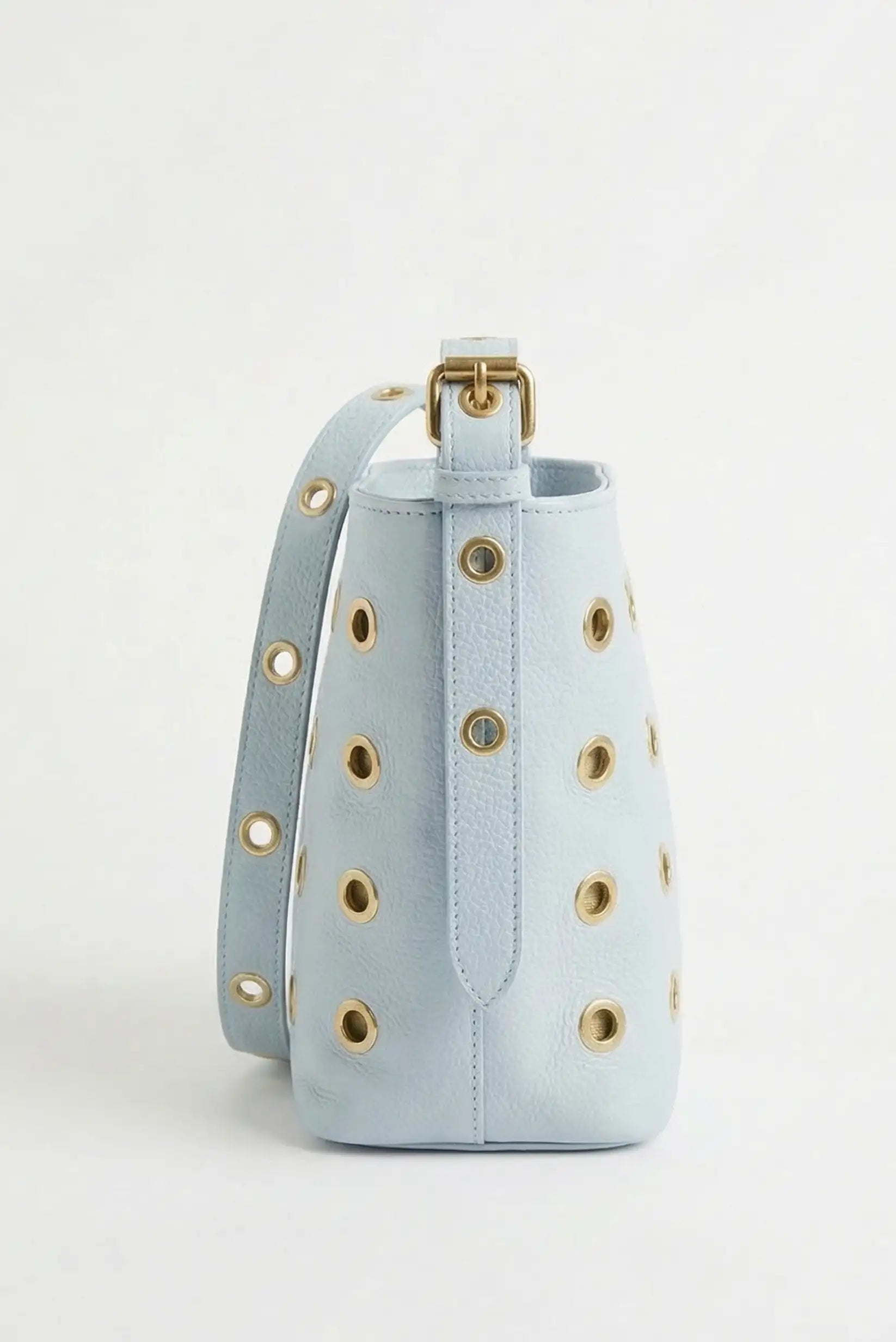 Bolso mediano azul pastel de piel con tachuelas doradas, diseño moderno y elegante.