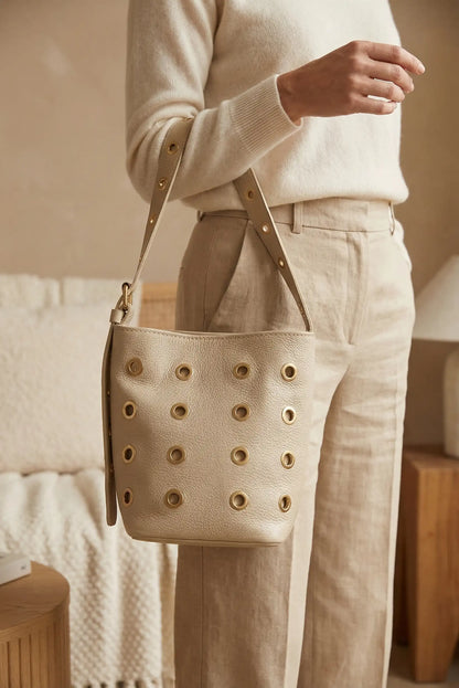 Bolso mediano beige de piel con tachuelas doradas, estilo casual femenino.