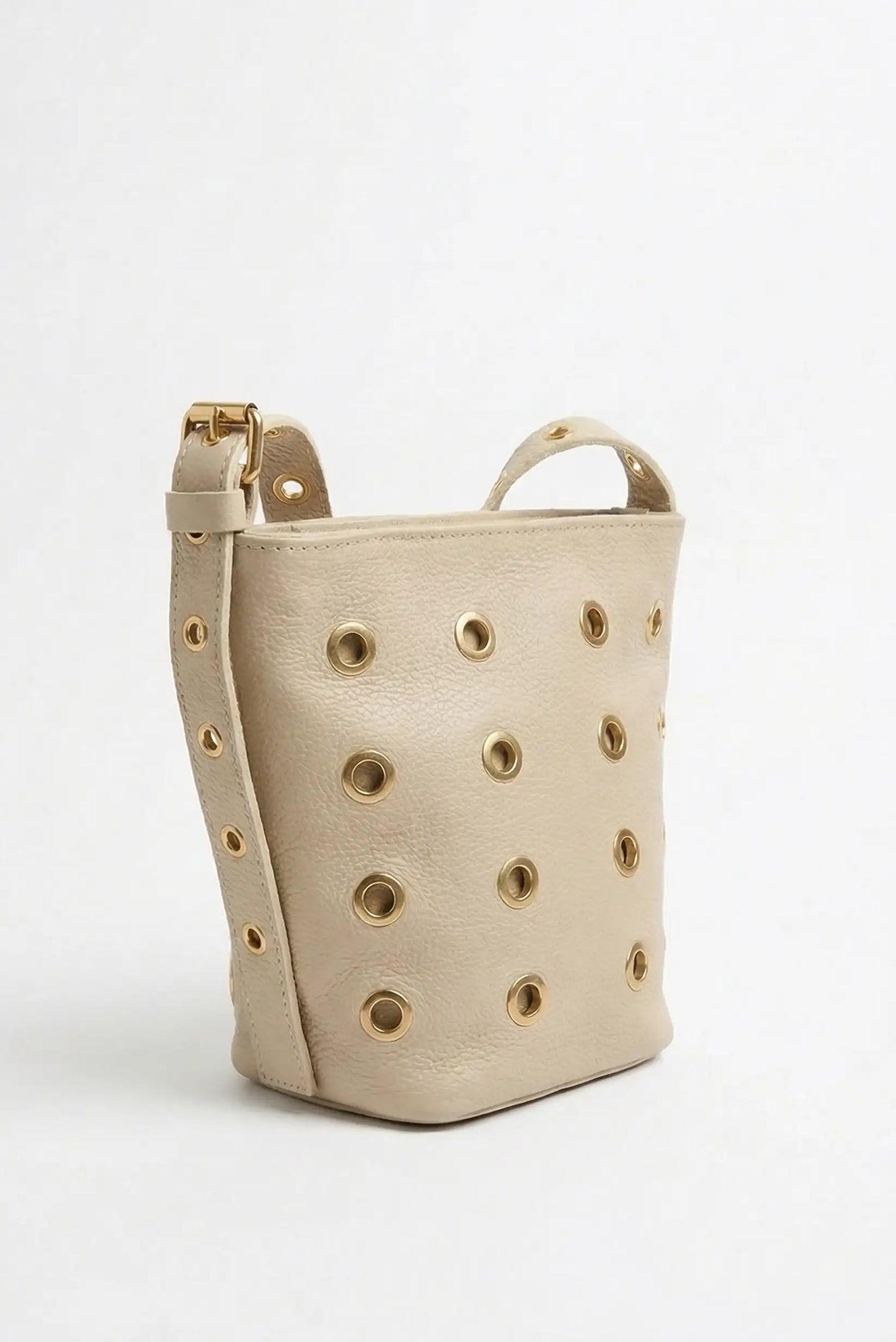 Bolso mediano beige de piel con tachuelas doradas y correa ajustable, estilo casual femenino.