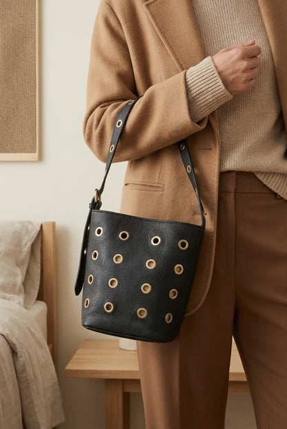 Bolso mediano negro de piel con tachuelas doradas circulares, estilo casual elegante.