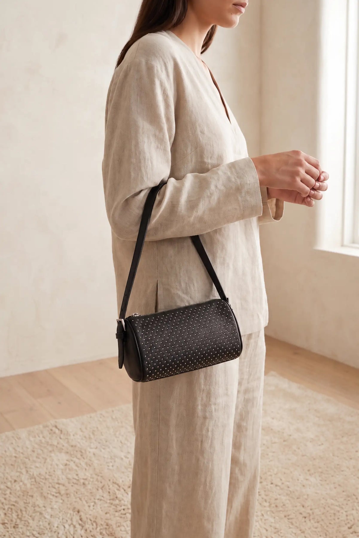 Mujer con conjunto de lino beige y bolso pequeño negro con tachuelas metálicas de CHICA del Sur
