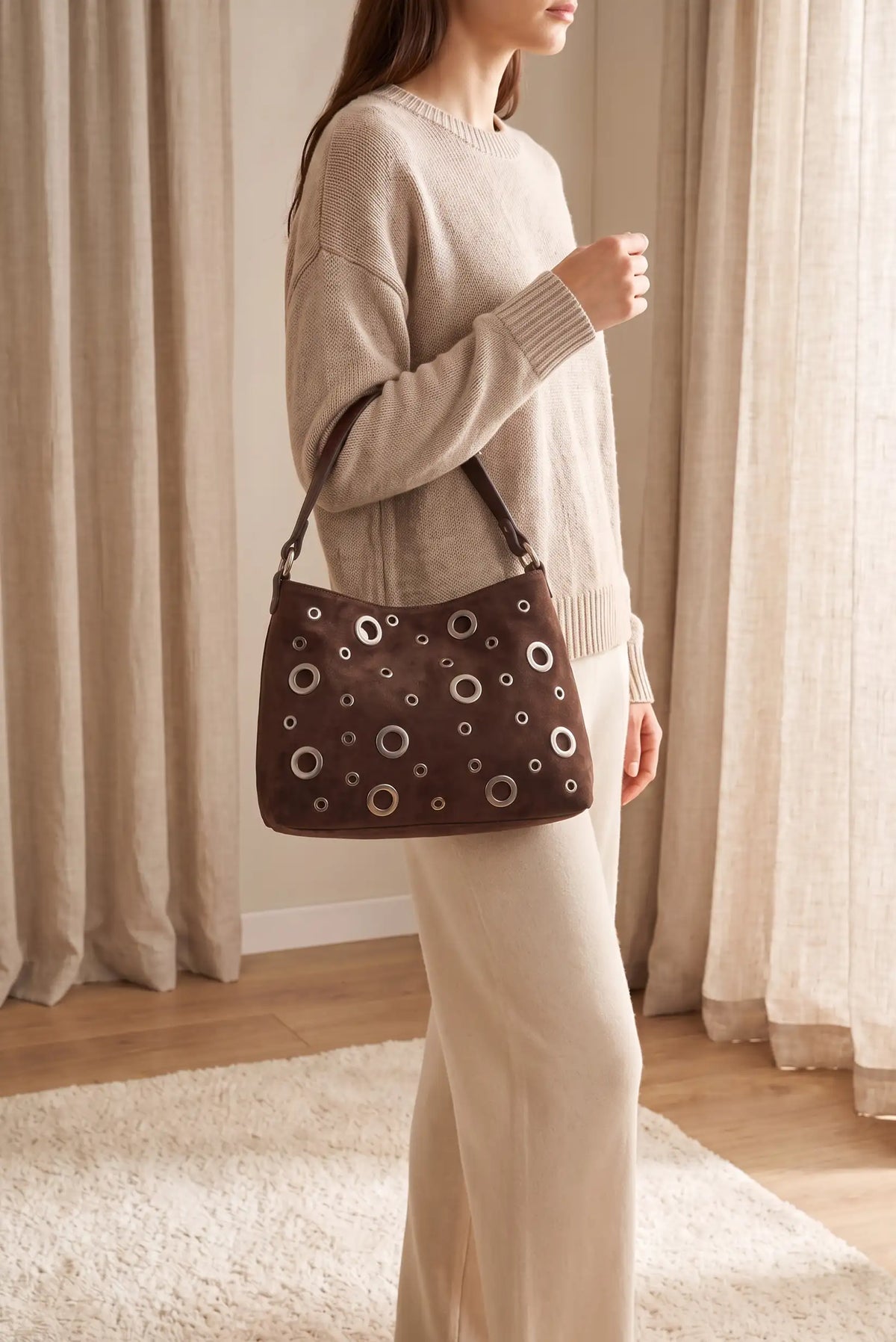 Mujer luciendo bolso marrón chocolate de CHICA del Sur con detalles metálicos circulares.