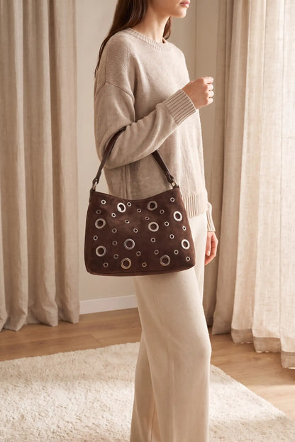 Mujer luciendo bolso marrón chocolate de CHICA del Sur con detalles metálicos circulares.