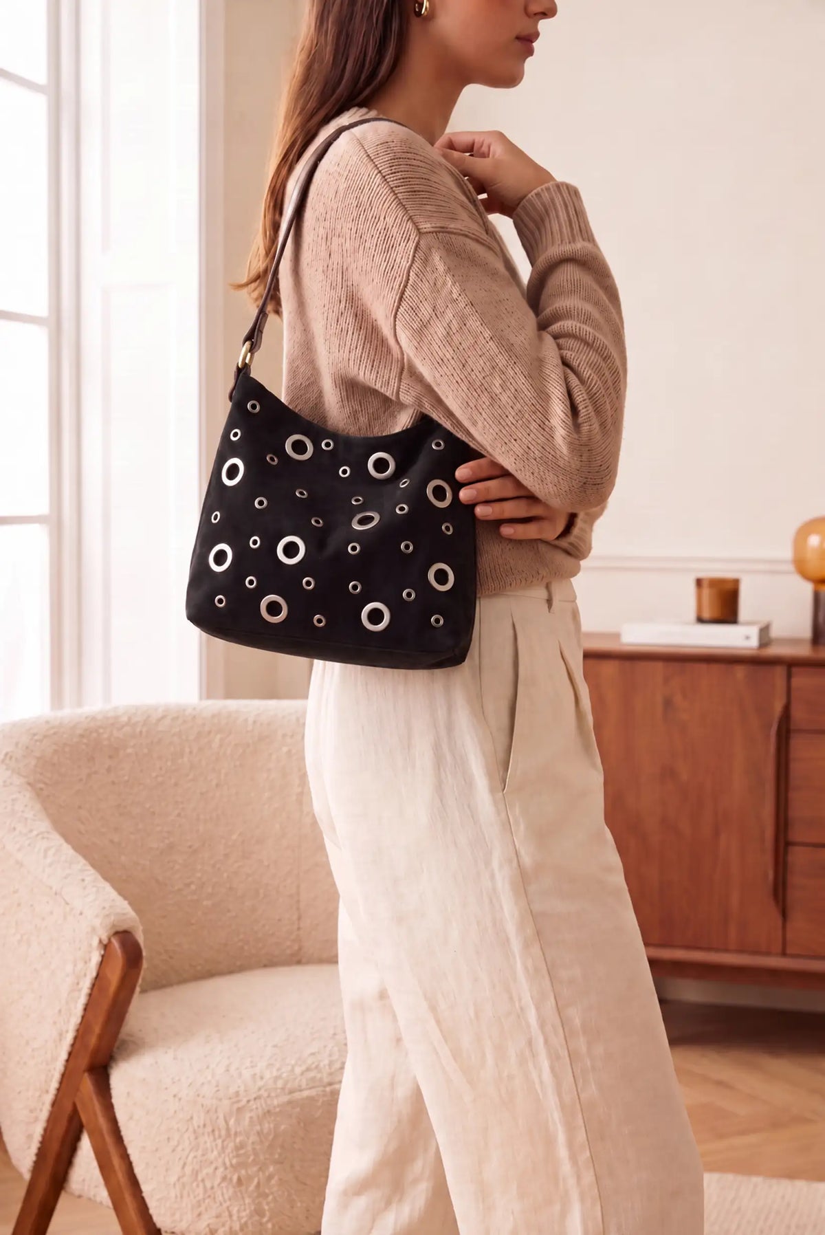 Mujer con bolso negro de CHICA del Sur con detalles metálicos circulares y pantalones beige.