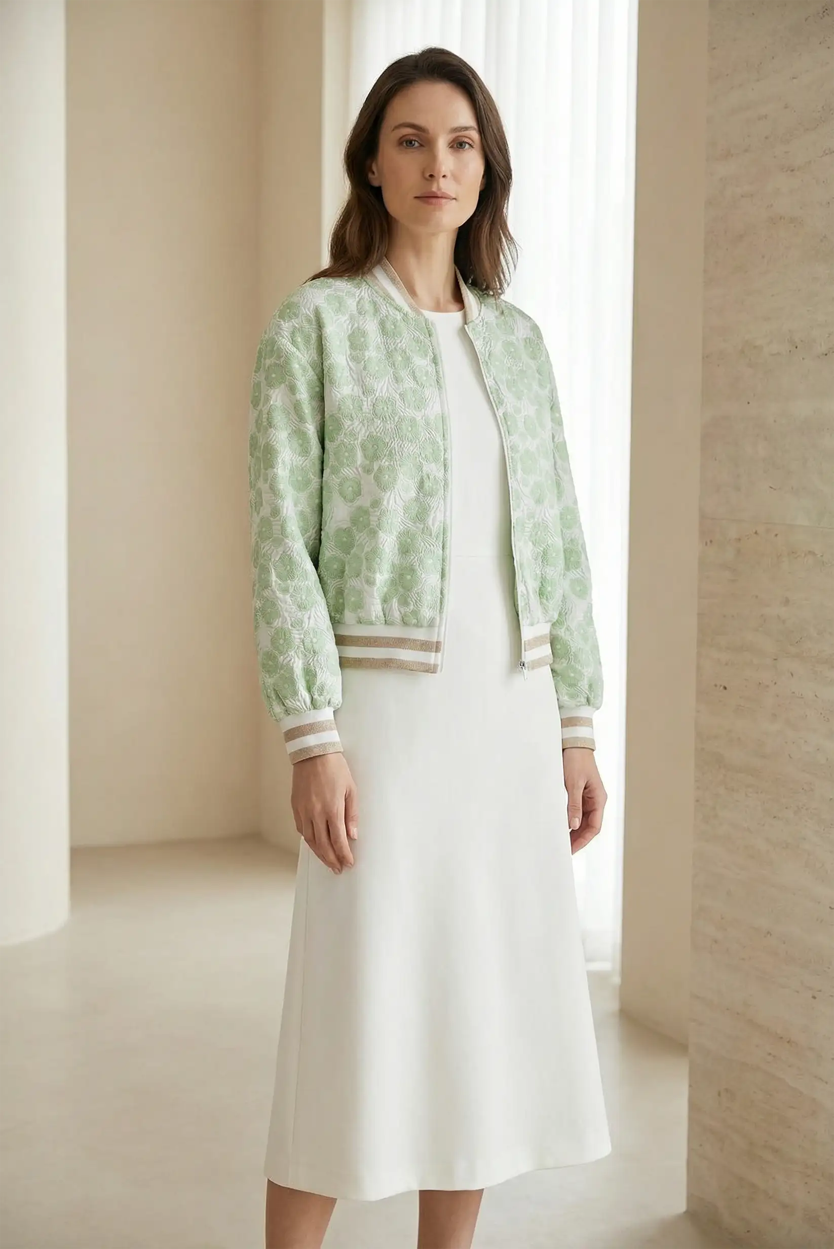 Mujer con chaqueta bomber verde clara de primavera y vestido blanco en ambiente minimalista.